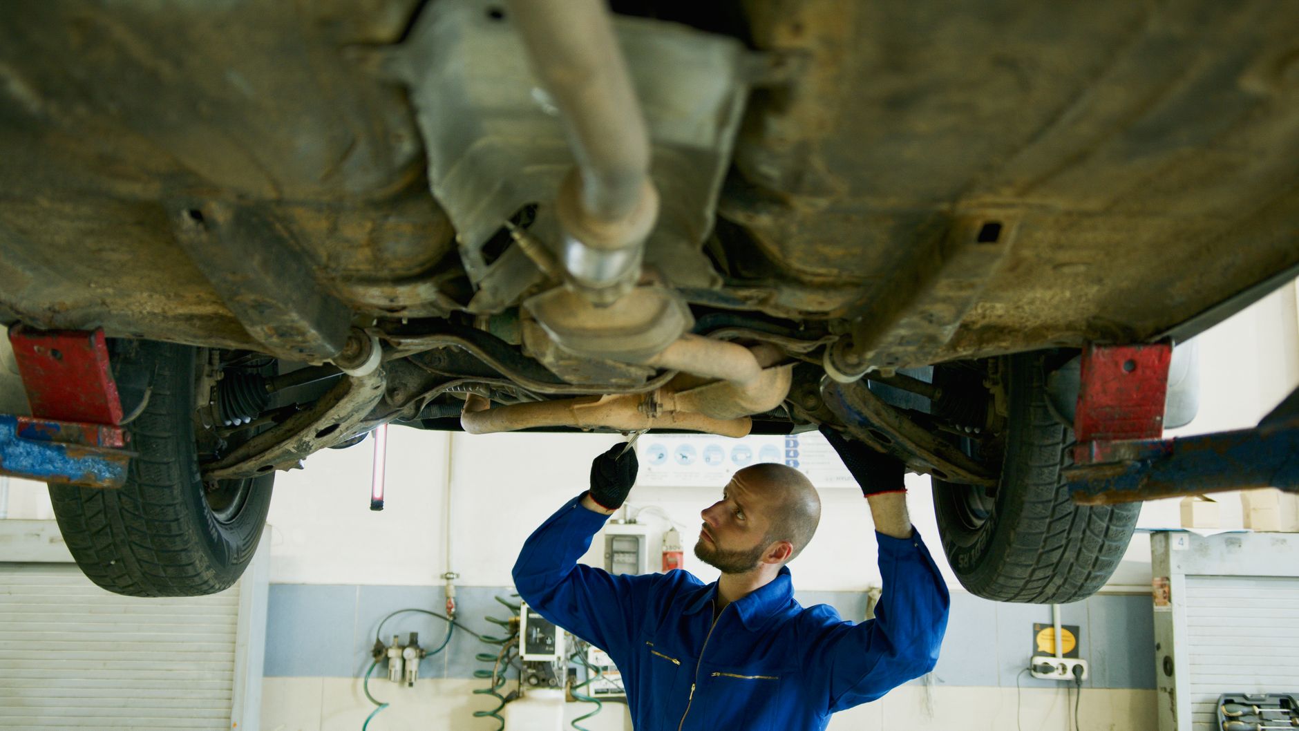 Mechanic examining the underside of a car in an auto repair shop for maintenance.